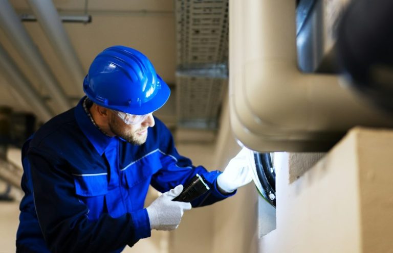 Ein Arbeiter in Blaumann und Helm untersucht eine Rohrleitung.