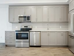 Moderne Küche mit grauen Schränken, Edelstahlgeräten und hellem Boden.