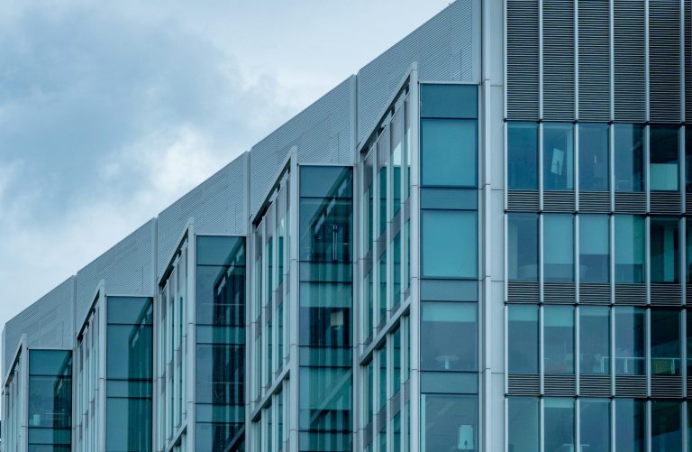 Moderne Bürogebäude mit Glasfassade und grauem Himmel im Hintergrund.